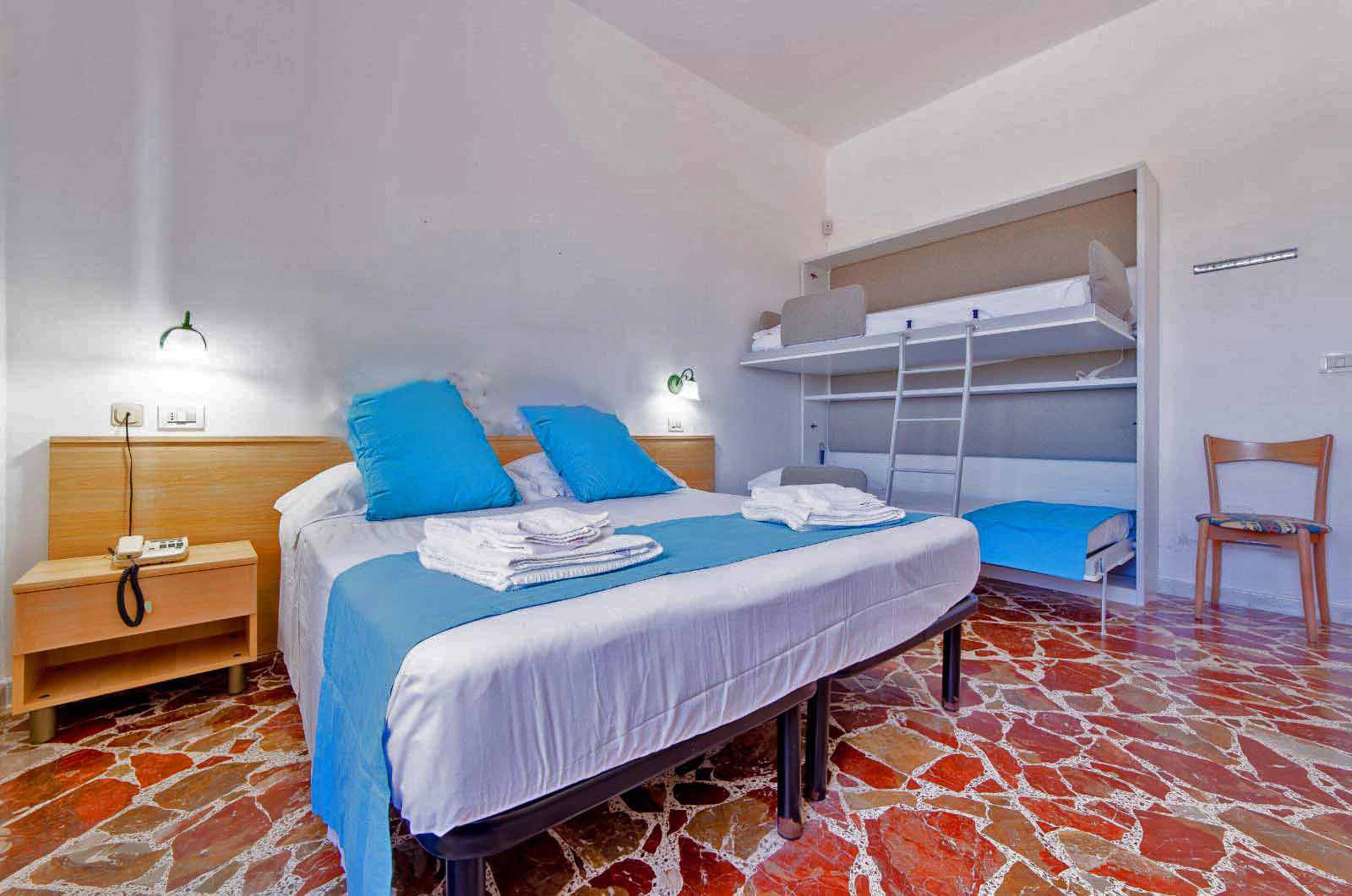 Un dormitorio con cama, mesita de noche, silla y literas.