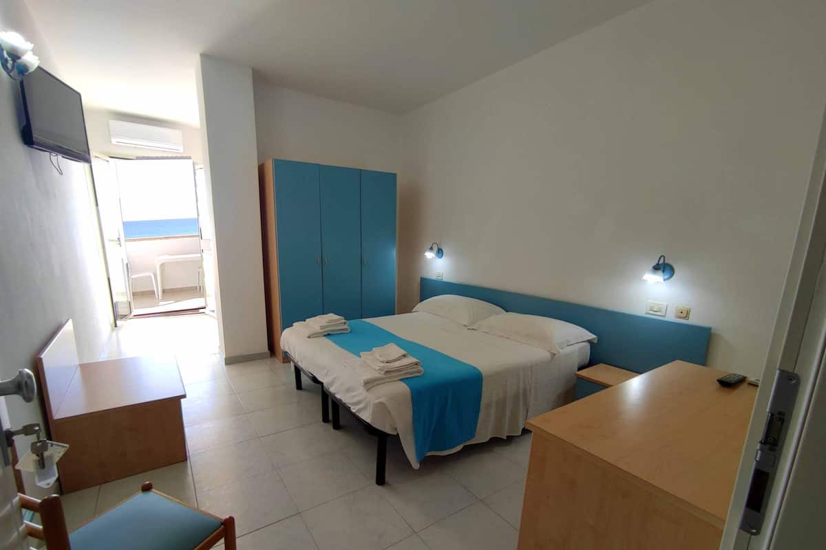 A hotel room with a bed, bedside tables, a desk, a chair, and a wardrobe.