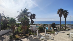 A rooftop terrace with a pool, palm trees, and a view of the sea. - Picchio Hotel Pescoluse (Salve)