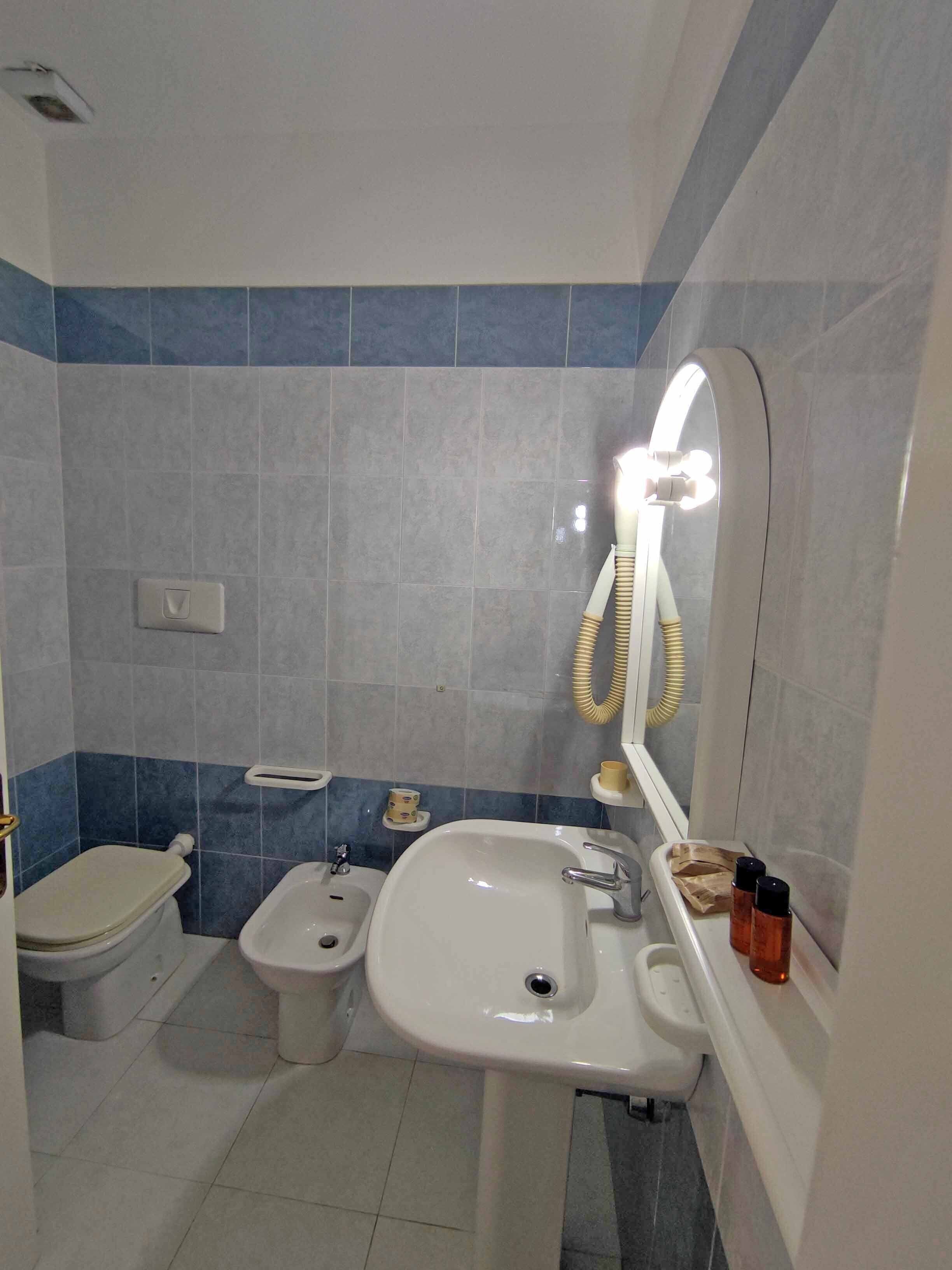 A bathroom with a toilet, bidet, sink, and a mirror with a light.