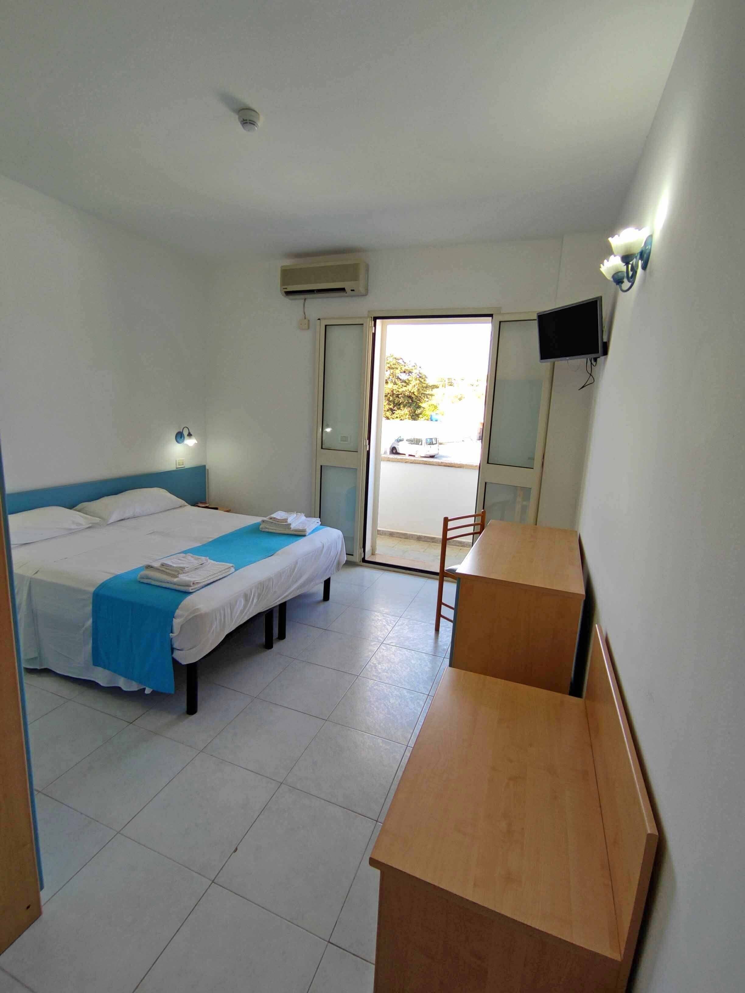 Une chambre d’hôtel équipée d’un lit, d’un bureau, d’une chaise, d’une télévision et d’une porte coulissante donnant sur l’extérieur.