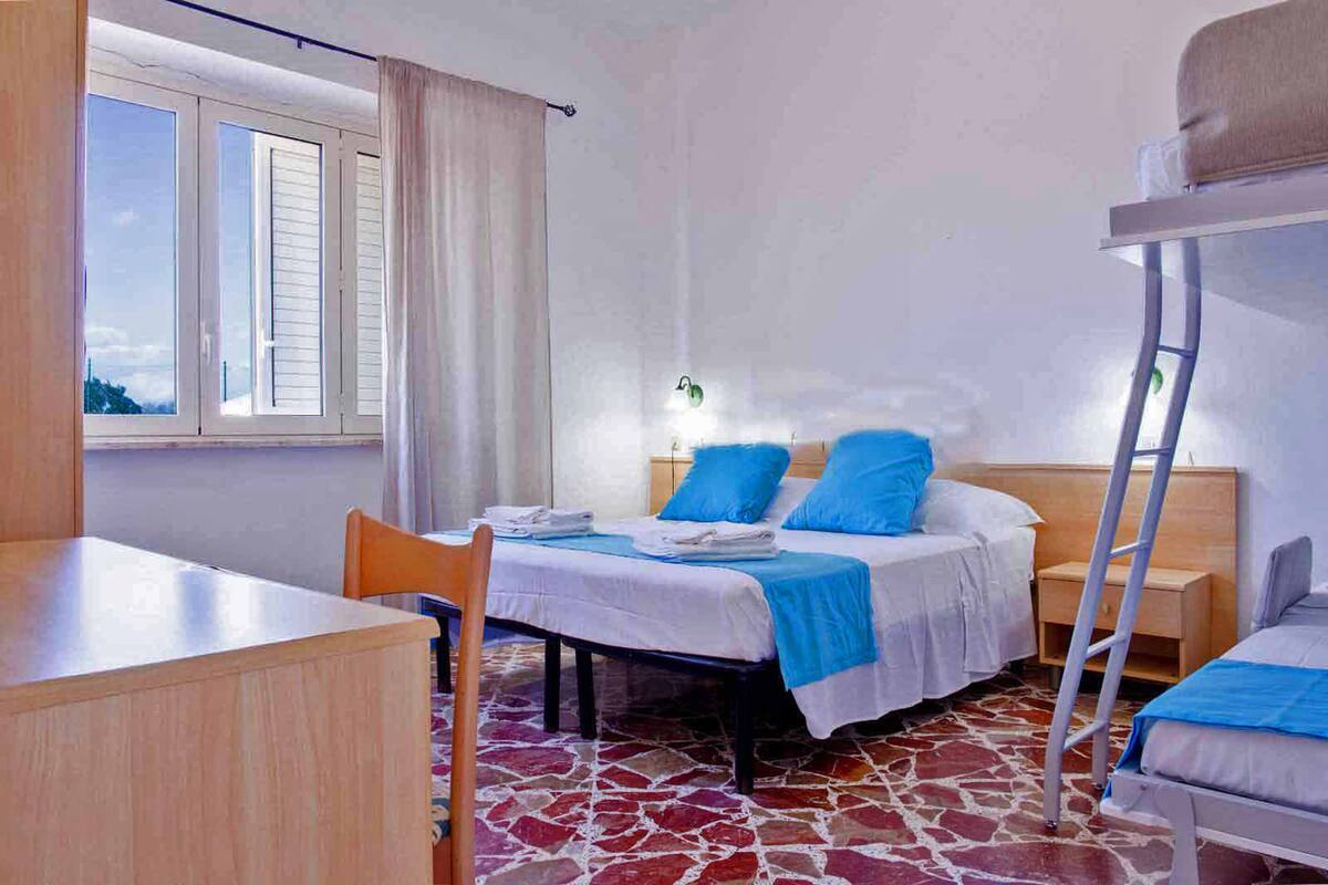 A room with a bunk bed, a desk, a chair, and a window with curtains.