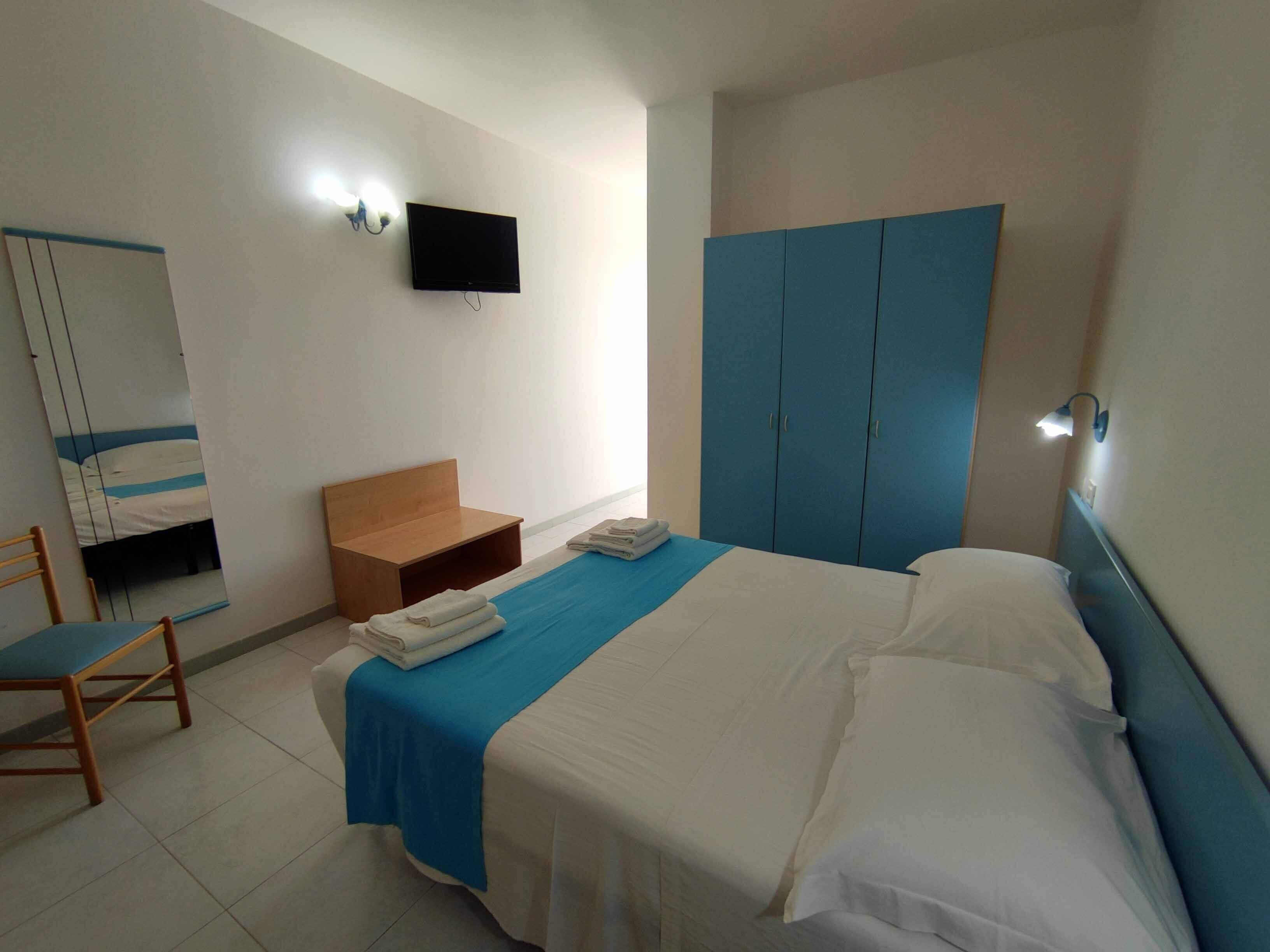 A hotel room with a bed, a desk, a chair, a wardrobe, and a TV mounted on the wall.