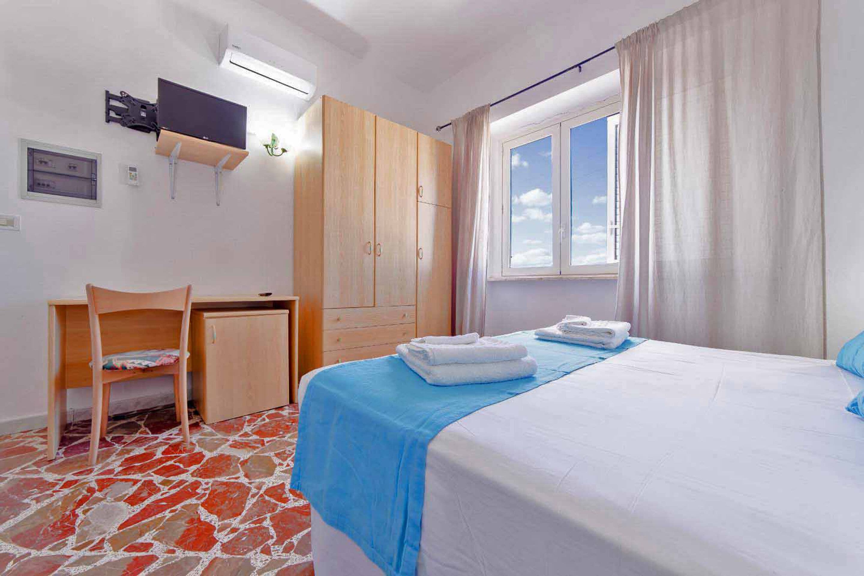 Une chambre à coucher comprenant un lit, un bureau, une chaise, une armoire et une fenêtre avec des rideaux.