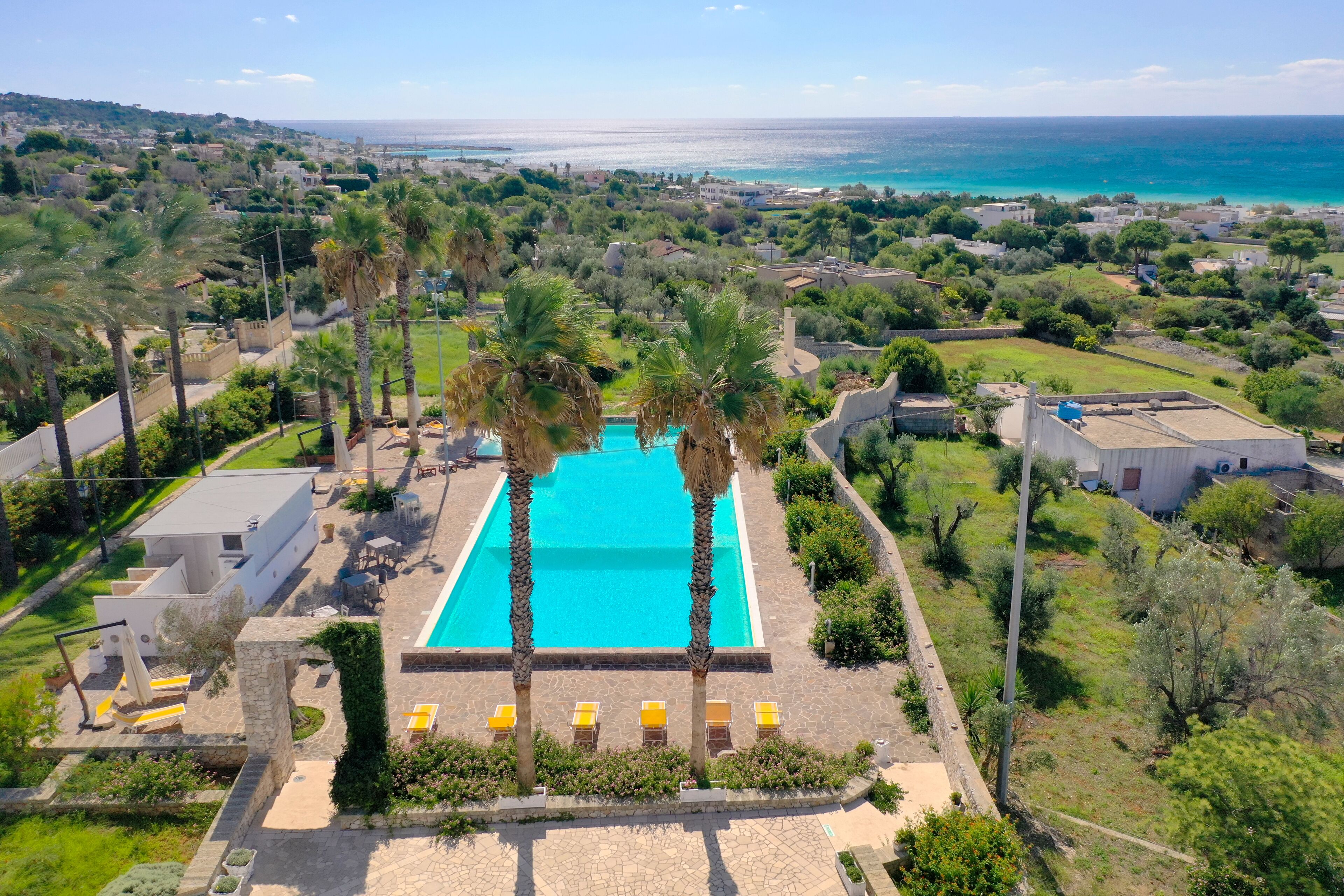 Un complexe hôtelier doté d’une piscine entourée de palmiers, d’un espace patio et offrant une vue sur l’océan.