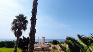 A tall palm tree in a landscaped area with a view of the sea and a stone structure in the background. - Picchio Hotel Pescoluse (Salve)