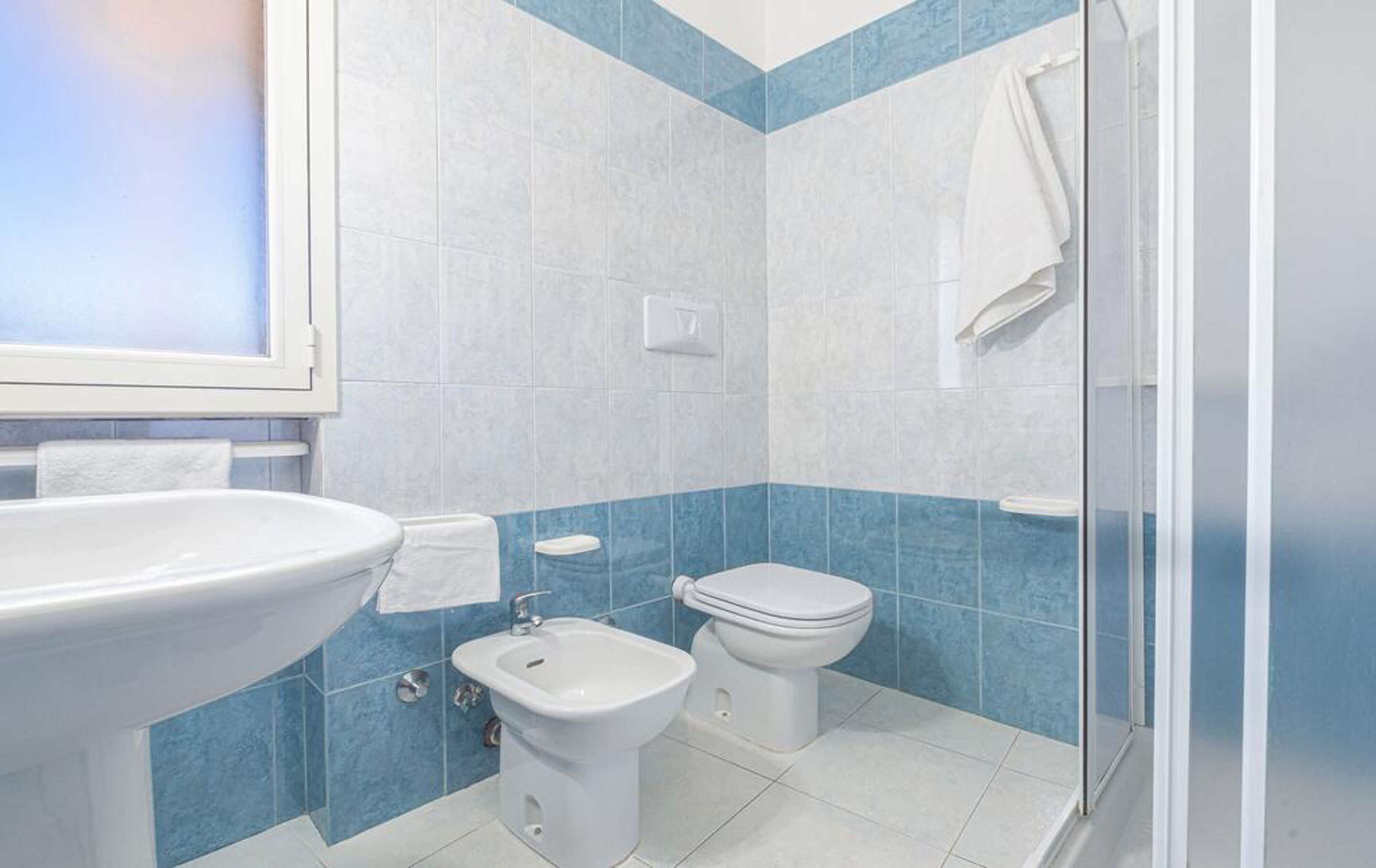 A bathroom with a sink, bidet, toilet, and a glass shower enclosure.