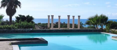 A swimming pool with a view of the ocean and palm trees.