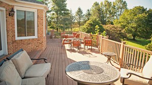 Un patio in legno con mobili da esterno, tra cui un tavolo rotondo e sedie, e un edificio in mattoni con ampie finestre.