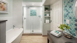 A modern bathroom with a bathtub, shower, and a vanity with a sink and shelves. - DOWNTOWN KEY WEST 2BED OCEANFRONT! (Key West)