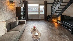 A living room with a sofa, a coffee table with a flower, a fireplace, a TV, and a staircase. - Stunning apartment in Bruinisse (Bruinisse)