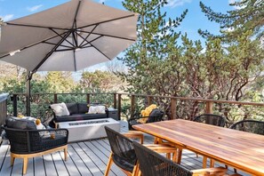 Een terras buiten met een houten tafel en stoelen, een bank en een grote parasol.