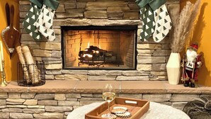 En öppen spis med en omramning av sten, ett brickbord med ett glas vin och julstrumpor.