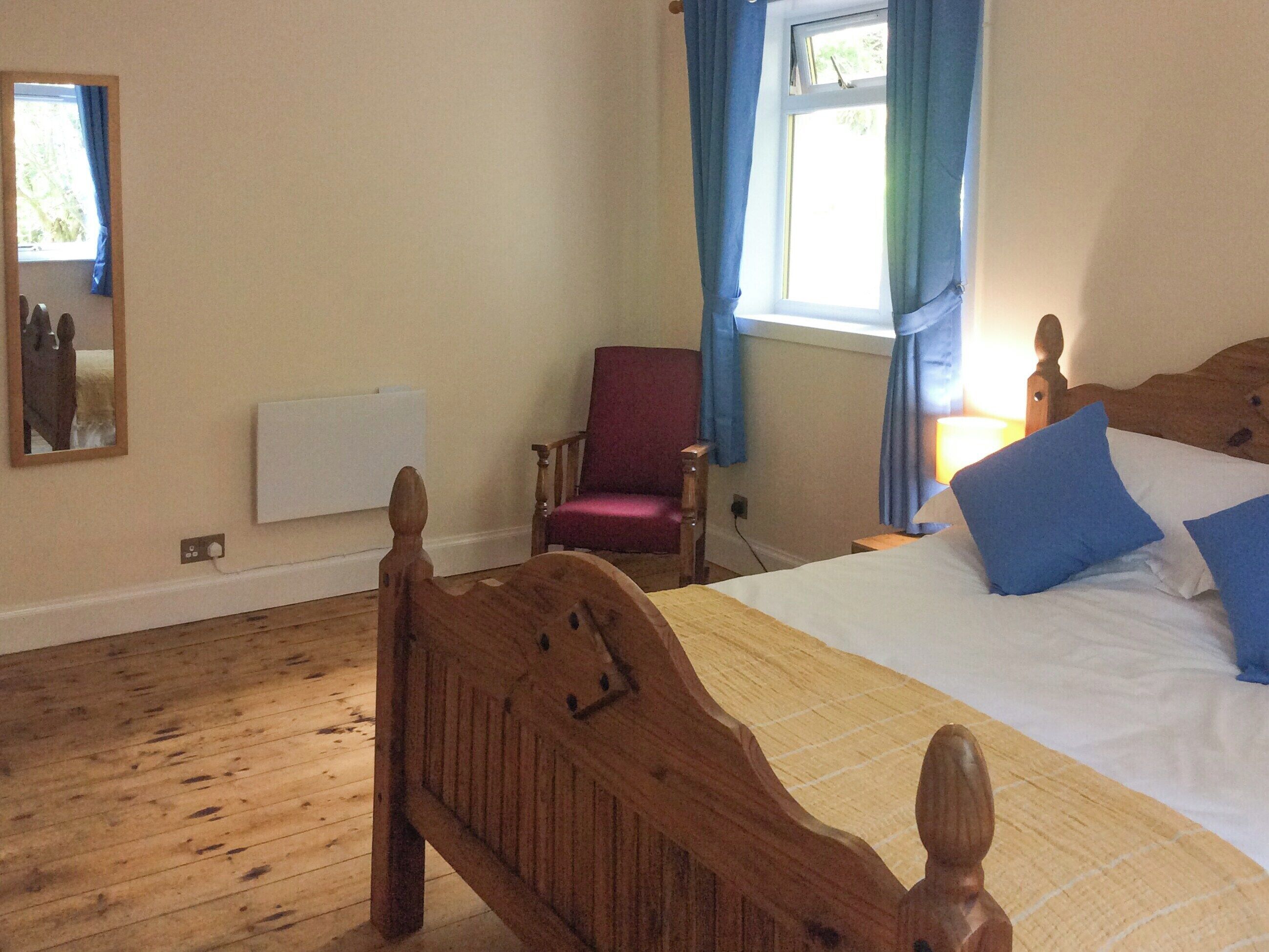 Una camera da letto con un letto di legno, una sedia rossa, una finestra con tende blu e uno specchio sul muro.