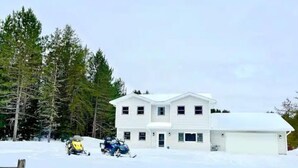 Ett vitt hus i två våningar med ett garage, omgivet av snö och träd.