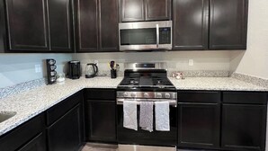 Una cocina con gabinetes de madera oscura, microondas de acero inoxidable, estufa a gas y encimeras de granito.