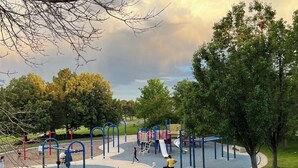 Un parque infantil con diversas estructuras de juego y un tobogán, rodeado de árboles y césped.