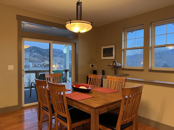 A dining area with a wooden table and chairs, a chandelier, and a view of mountains through large windows.