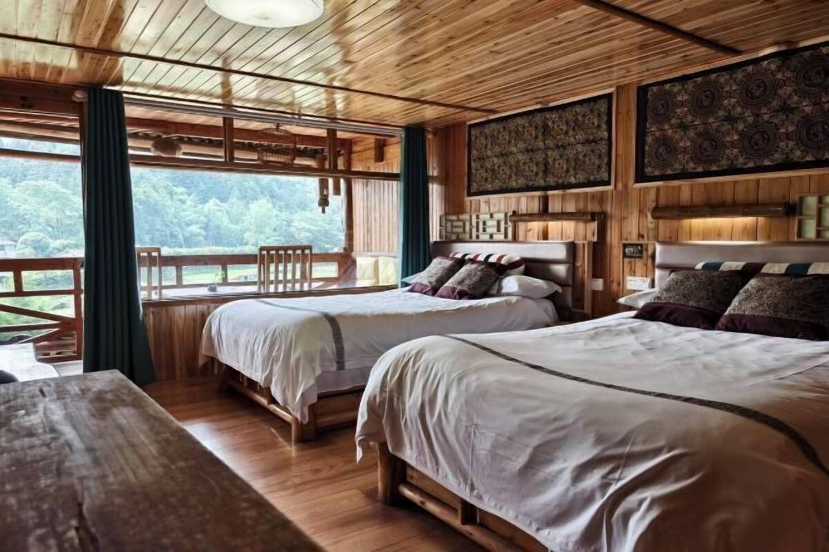 A wooden cabin-style bedroom with two beds, a large window, and a view of the outdoors.