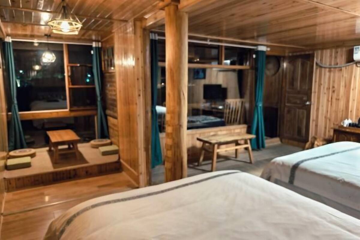 A wooden cabin with two beds, a small table, and a window with curtains.