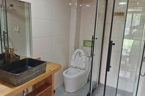 Ein Badezimmer mit einem Holzbadezimmermöbel, einer weißen Toilette, einer Duschkabine aus Glas und einem sichtbaren Schild an der Wand.