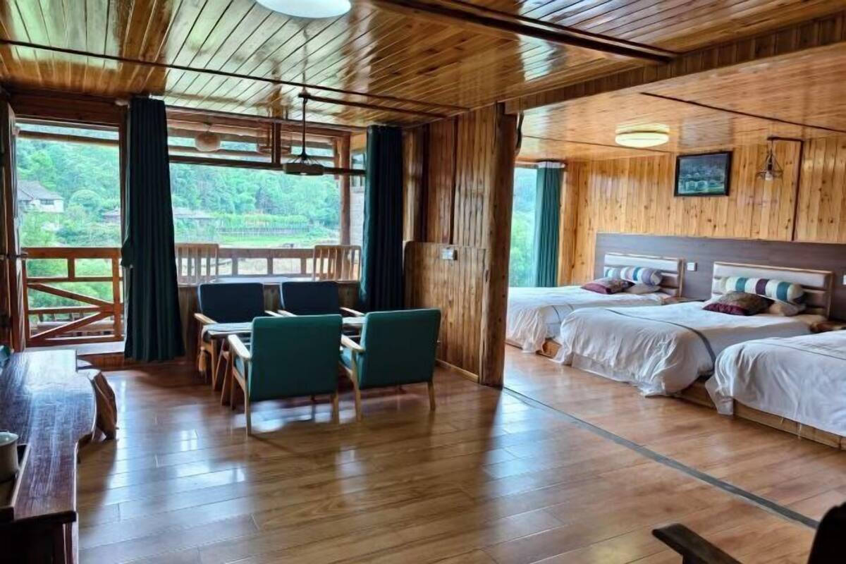 A wooden cabin with a dining area, two beds, and a view of greenery.