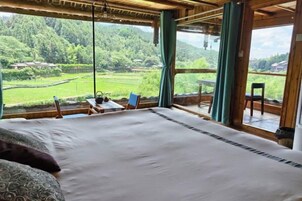 Un dormitorio con una cama grande, vistas a un paisaje verde y una pequeña mesa con sillas.