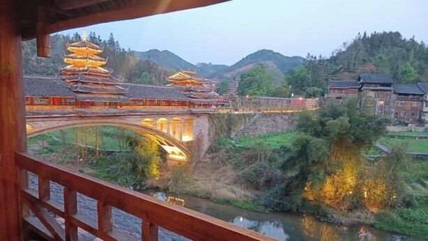 A traditional Chinese architectural structure with multiple tiers, a bridge, and a river. - Wangqiao Tower Boutique Guesthouse (Sanjiang)