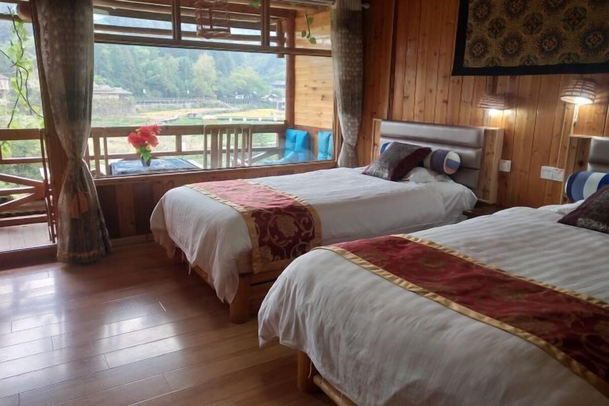 Ein Zimmer mit zwei Betten, Holzboden, einem großen Fenster mit Blick und einer Holzzielenge.