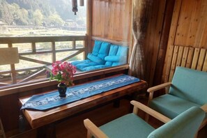 Eine Holzhütte mit einer Bank und einem Stuhl, einem Tisch mit blauer Decke und einer Vase mit rosa Blumen.