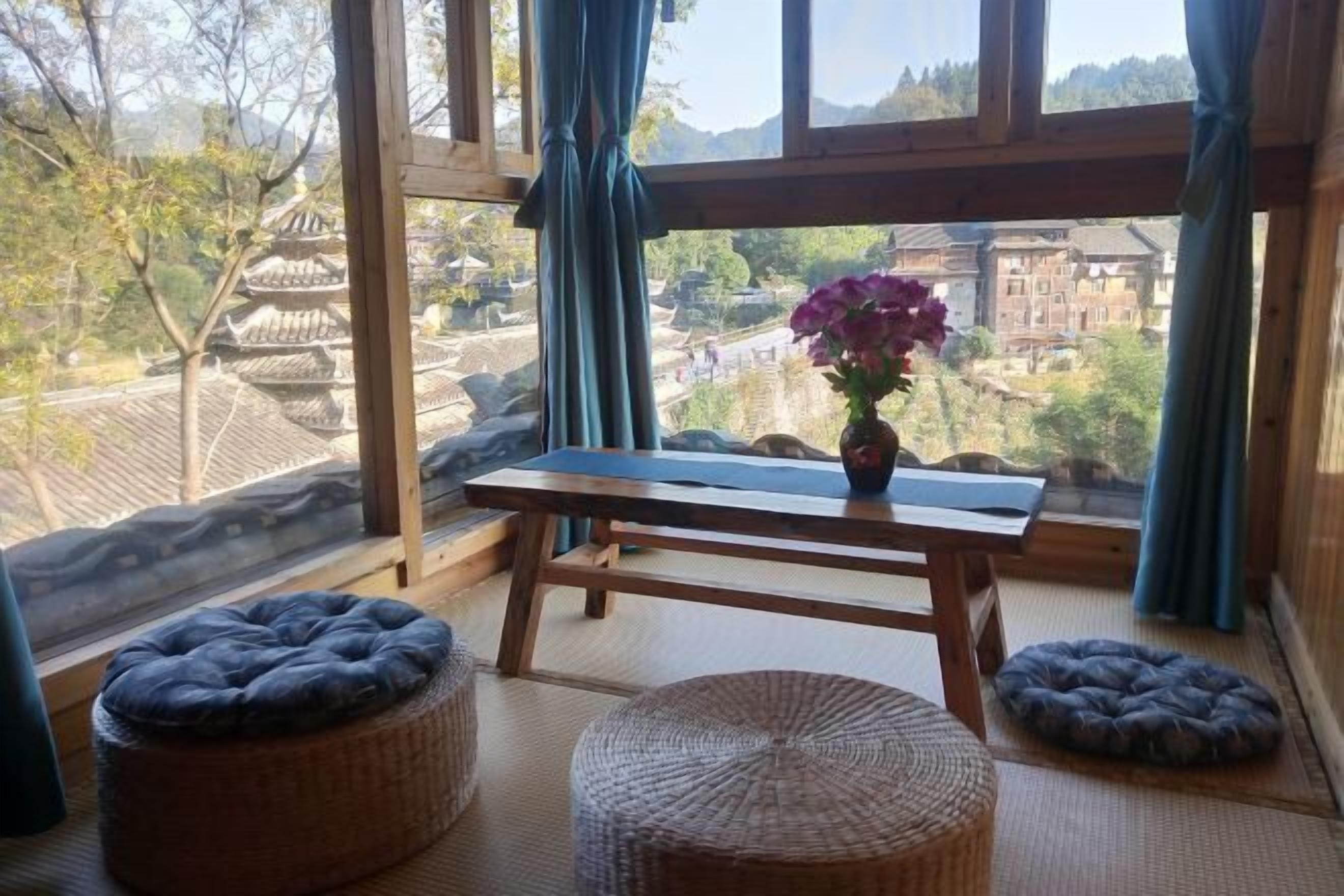 A room with tatami mats, a wooden table with a vase of flowers, and a view of traditional architecture.
