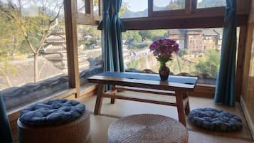 A room with tatami mats, a wooden table with a vase of flowers, and a view of traditional architecture.