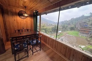 Ein Essbereich mit Holzboden, einem Tisch und Stühlen, große Fenster mit Blick auf eine ländliche Gegend.