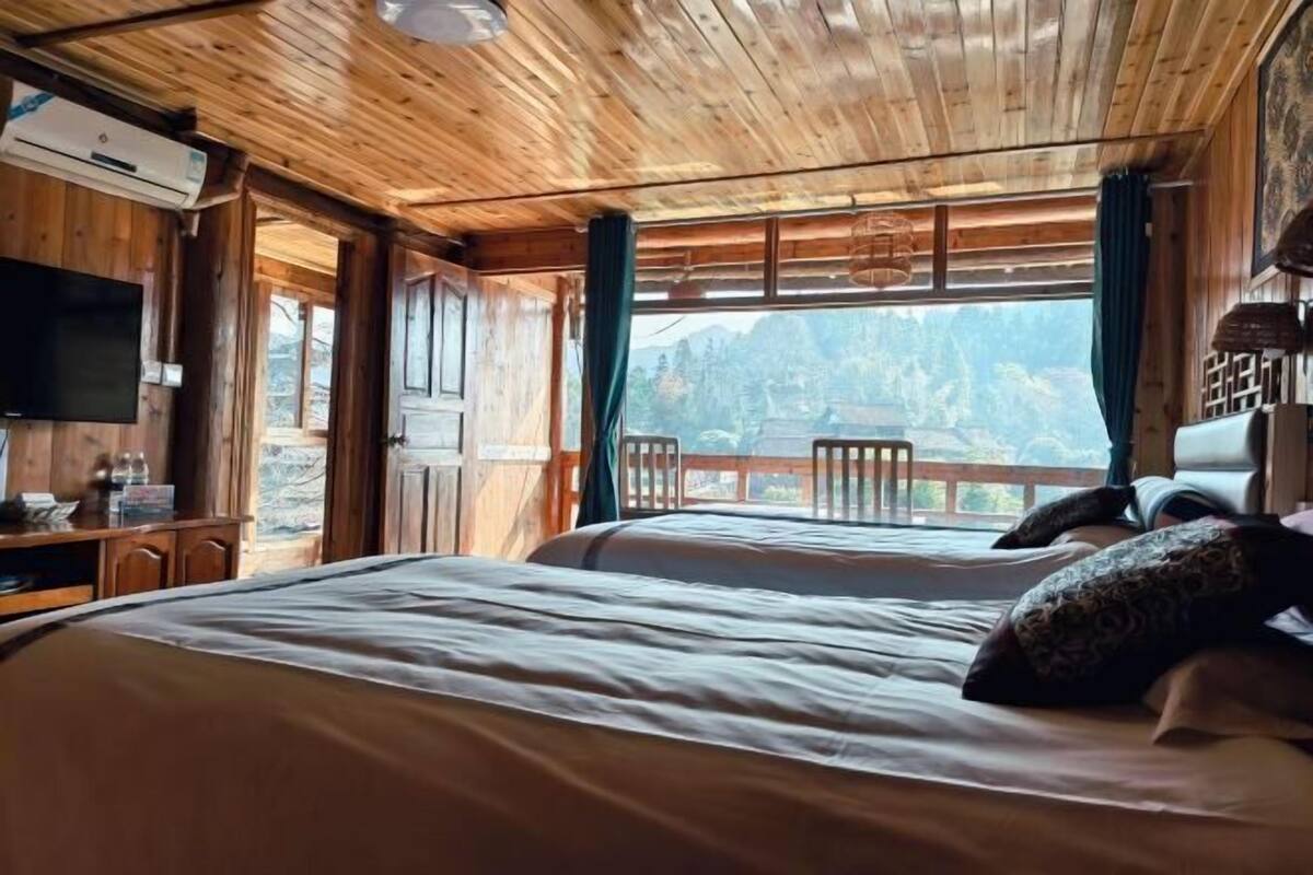 A wooden cabin bedroom with a bed, a desk, and a TV.