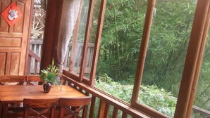 A wooden dining table with chairs, a potted plant, and a view of bamboo forest through large windows. - Wangqiao Tower Boutique Guesthouse (Sanjiang)
