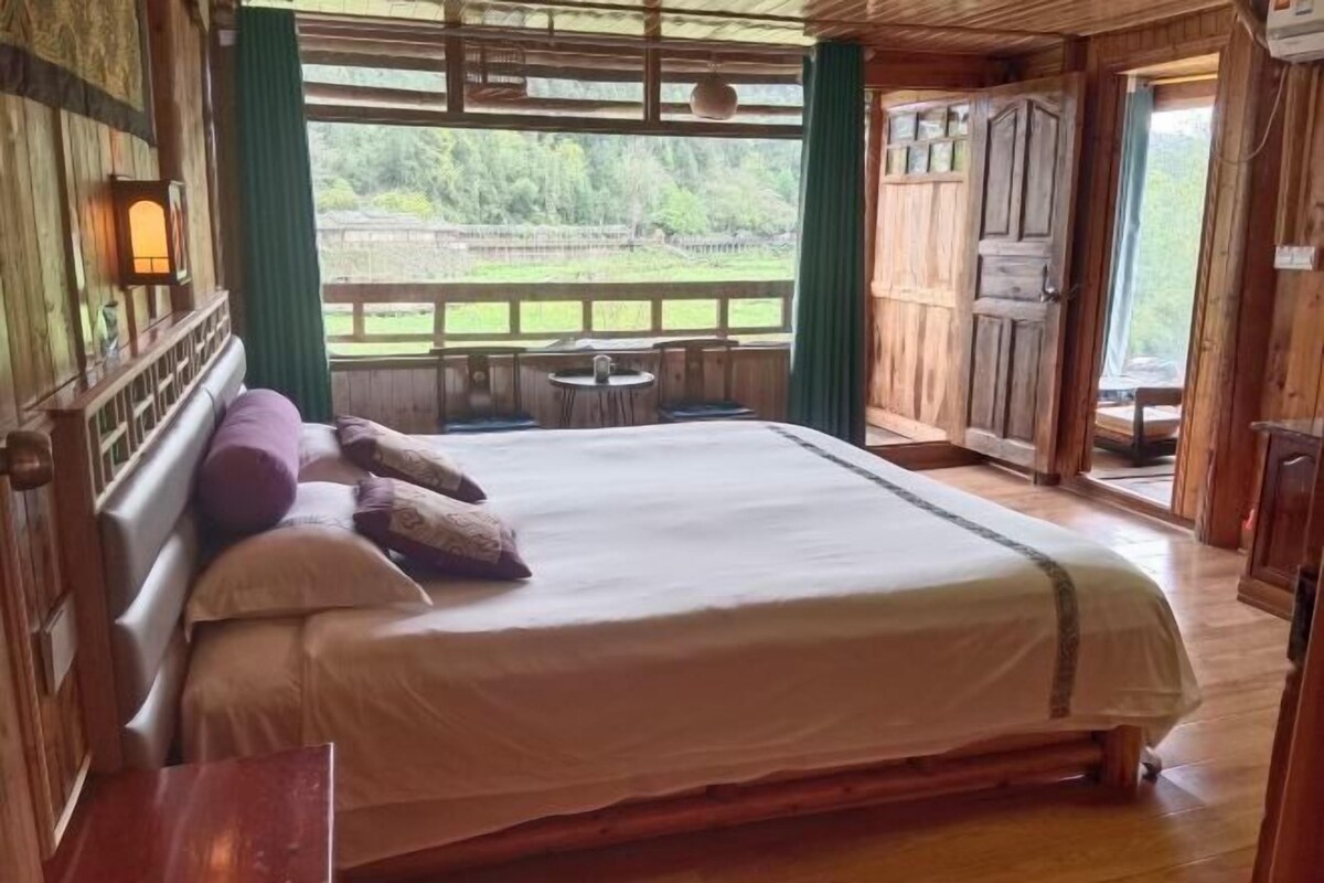 Ein Schlafzimmer einer Holzhütte mit einem Bett, einem kleinen Tisch und Blick ins Freie.
