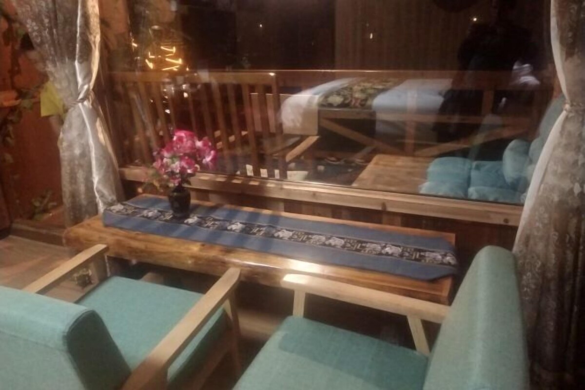 Ein Zimmer mit einer hölzernen Bank, einem kleinen Tisch mit einem gemusterten Tischläufer und einem Sessel mit Kissen.
