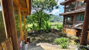 A wooden staircase leading to a balcony overlooking a lush garden and a mountain view. - Wangqiao Tower Boutique Guesthouse (Sanjiang)