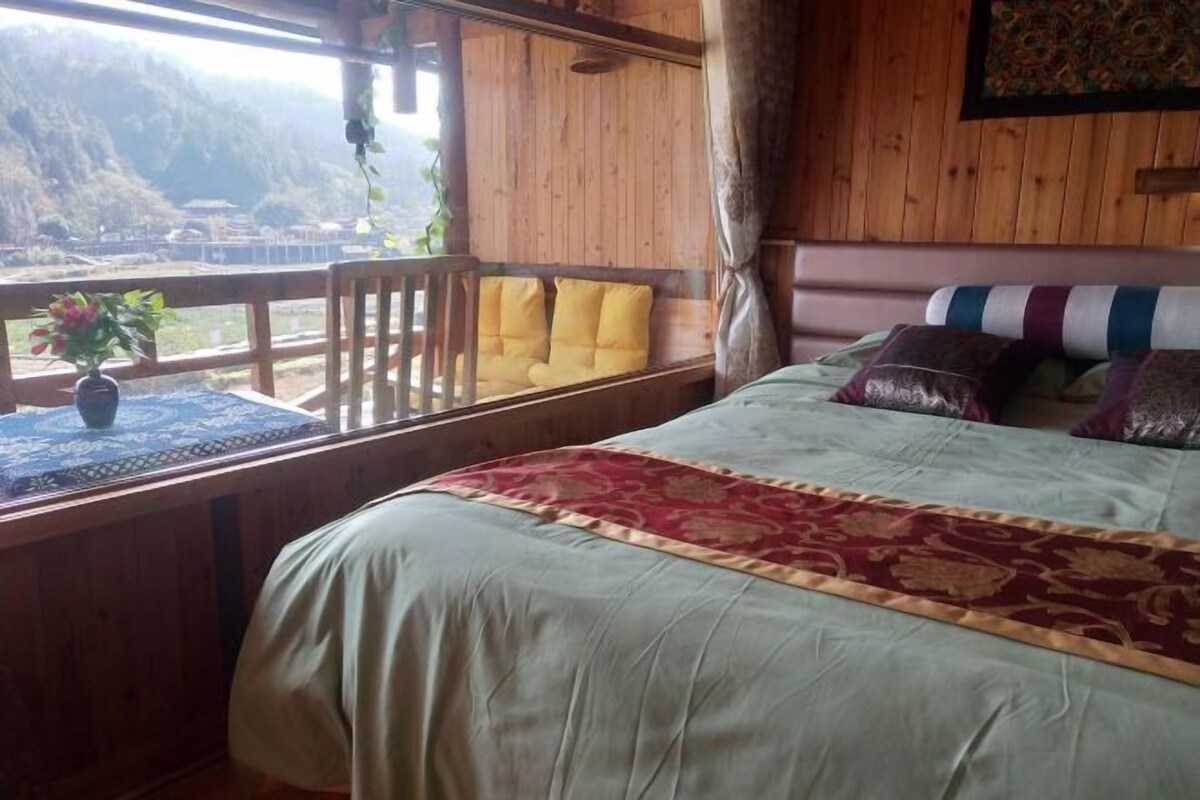 Ein Zimmer aus Holz mit einem Bett, einem Fenster mit Blick auf eine Berglandschaft und einem kleinen Tisch mit einer Blumenvase.