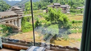 A room with a large window overlooking a traditional bridge and lush greenery. - Wangqiao Tower Boutique Guesthouse (Sanjiang)