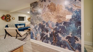 A living room with a blue sofa, a coffee table, and a decorative wall with a nature-themed mural. - Washington DC Apartment at Rock Creek Park! (Washington)