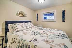A bedroom with a bed, a nightstand, a wall-mounted light fixture, and a window with a view of trees. - Washington DC Apartment at Rock Creek Park! (Washington)