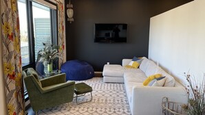 Ein modernes Wohnzimmer mit einer Couch, einem grünen Sessel, einem blauen Sitzsack und einem gemusterten Teppich.