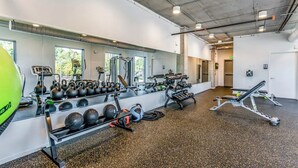 Ein Fitnessraum mit Trainingsgeräten, einem großen Spiegel und Blick auf Bäume.