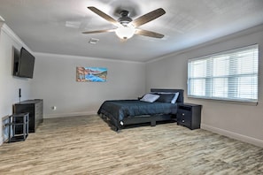 A bedroom with a bed, a ceiling fan, a TV, and a window with blinds.