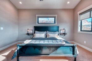 A bedroom with a bed, two bedside tables, a window, and a view of a cityscape.