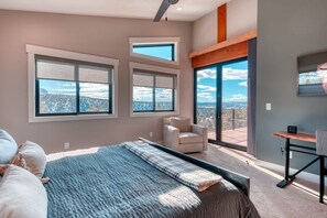 Une chambre avec un grand lit, deux fenêtres donnant sur un beau paysage, une chaise et un bureau.