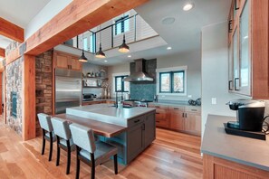 Una cocina moderna con una isla central, vigas de madera, detalles de piedra y una chimenea de piedra.
