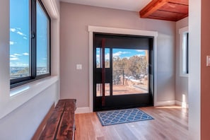 Una habitación con un ventanal grande, una puerta que da al exterior y un banco de madera.