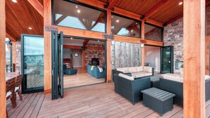 A spacious indoor area with a wooden deck, a stone fireplace, and a large glass door leading to an outdoor deck. - Panoramic Views & Hot Tub near Zion/Bryce (Orderville)